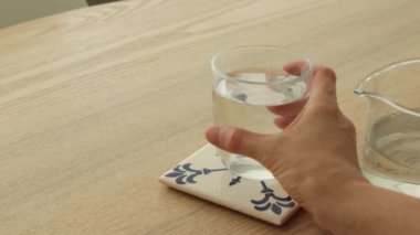 Kadın eli modern mutfak estetiğinde masadan bir bardak su alıyor.