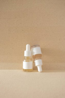Bej arka planda minimalist modern serum şişeleri. Cilt bakım ürünü kozmetik model, dikey 