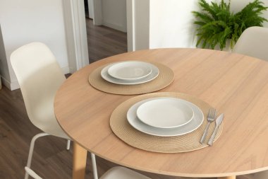 Modern yurt odasındaki ahşap masada asgari masa. Yuvarlak bir paspasın üzerinde çatal ve bıçaklı beyaz seramik tabaklar.