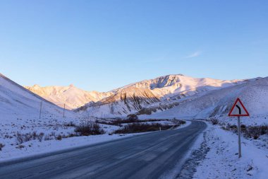 Buzlu kış yolu gün doğumunda dağlarda.