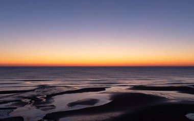 Şafak vakti kıyıya yakın denizin pürüzsüz kırmızı ufku.
