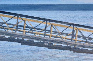 Abstract double exposure of yellow and black foor bridge over background of rippled water and a forested shoreline.