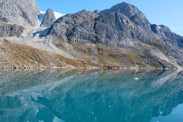 Doğu Grönland, Skoldungen yakınlarındaki Dronning Marie Dal yakınlarında fiyordun durgun sularındaki çıplak kaya, kaya ve buzul yansımaları.