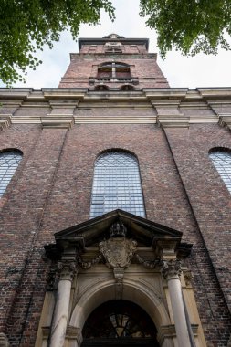 Kopenhag, Danimarka 3 Ekim 2023 - Vor Frieisers Kirke, Christiania girişinin önünde dikilirken çan kulesi ve çan kulesine bakarken yeşil yapraklarla çerçevelenmiş