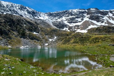 Estanyo Gölü 'nün berrak suları - Sorteny Doğa Koruma Alanı - taze karla kaplı dağların altında yer alır.