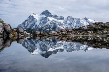 Smooth surface of small lake on Huntoon Point, Washington provides a mirror-like image of Mount Shuksan freshly covered with snow. clipart