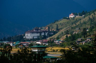 Paro Dzong 'un heybetli yapısı Paro şehrinin üzerinde yükseliyor. Yukarıda, Bhutan Ulusal Müzesi batan güneşin son ışınlarını yakalıyor.