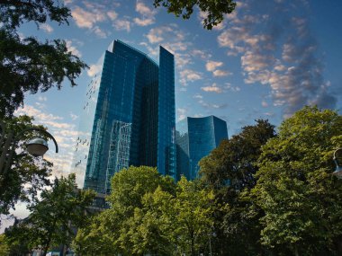 Frankfurt 'ta bir gökdelen. Önünde ağaçlar olan bulutlu bir gökyüzü.
