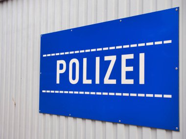 Üzerinde polis yazan gri metal bir arka planda büyük mavi bir tabela.