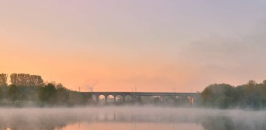 Arka planda bir köprü ve göllü bir manzaranın yakın çekimi.