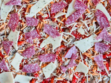 Peynirli, salamlı, ton balıklı fırınlanmamış bir pizzanın yakın çekimi.