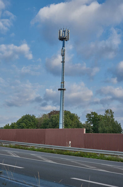 A vertical shot of a highway with protection wall and a telecommunications tower on a cloudy day
