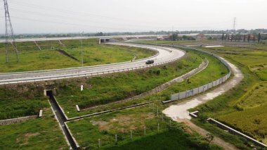 Endonezya, Central Java 'daki Jogja-Solo otobanının göz kamaştırıcı hava fotoğrafı. Görüntü, yemyeşil manzaralar, tarım alanları ve canlı kırsal alanlarla çevrili modern otoyol altyapısını vurguluyor. Taşıma için mükemmel.