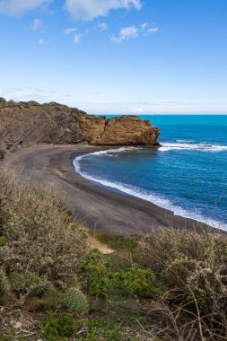 Kara kum plajı ve volkanik kayalıklar.