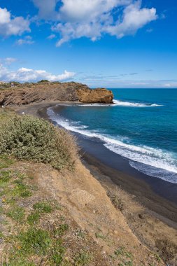 Kara kum plajı ve volkanik kayalıklar.