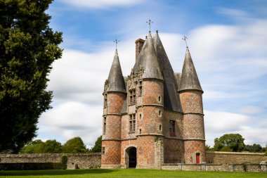 XII. Louis tarzında dört dairesel kırmızı ve siyah tuğlalı kulesiyle Carrouges Kalesi 'nin kapısının uzun pozlu görüntüsü.