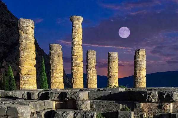 Temple of Apollo at Delphi in Greece during blue hour against the full moon.