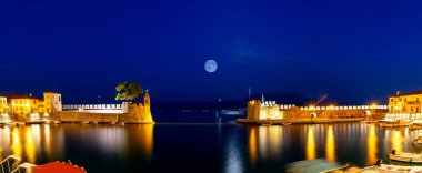 Mavi saatte dolunaya karşı Nafpaktos limanı panoraması.