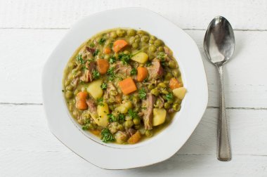 Yukarıdan izole edilmiş beyaz ahşap arka planda bezelye güveci tabağı