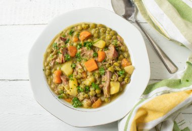 Yukarıdan izole edilmiş beyaz zemin üzerinde bir çorba tabağı üzerindeki bezelye yahnisi.