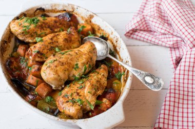 Fırında tavuk göğsü ve beyaz arka planda izole edilmiş güveç kabında İtalyan sebzeleri.