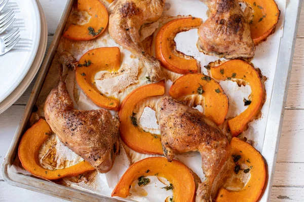 Stock image Oven roasted chicken legs with red kuri squash on a baking sheet. Served on white wooden background from above