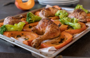 Düşük karbonhidrat ya da ketojenik diyet için leziz sağlıklı bir yemek. Kızarmış fırında tavuk budu, kırmızı kuri kabağı ve brokoli. Pişirme çarşafında yemeye hazır, arka planda bulanık ön manzara