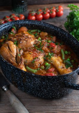 Lezzetli ve sağlıklı kahverengi tavuk güveci. Pişmiş, İtalyan usulü domatesli, dolmalık biberli, soğanlı, otlu, yeşil fasulyeli, patatesli ve bezelyeli. Tahta masadaki kırsal bir tencerede servis edilmiş..