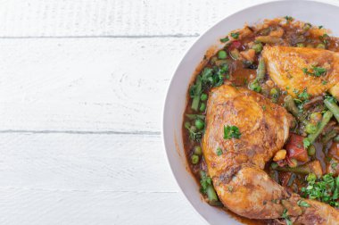 Sebze, patates ve baklagillerle pişirilmiş tavuk budu. Beyaz arka planda izole edilmiş ve fotokopi alanı olan bir kasede.