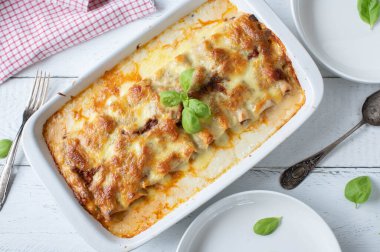 Cannelloni ile doldurulmuş makarna güveci bolonez ve mozzarella peyniri soslu beyaz ahşap arka planda bir güveç kabında. Düz yatıyordu