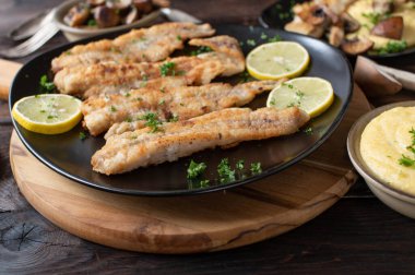 Pan fried fish with creamy polenta and mushrooms fried in butter on a rustic and wooden table for dinner or lunch. Closeup and front view