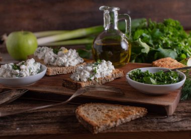 Roasted sourdough bread with cottage cheese salad on wooden table with herbs and olive oil carafe, mediteranean food