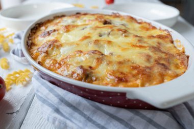 Whole and closed casserole with cheese in a oval casserole dish on white kitchen table background. Closeup and front view
