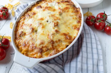 Noodle casserole with bolognese and bechamel sauce with cheese topping in a casserole dish on white table