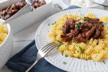 Chicken ragout or stew with buttered pasta and parmesan cheese,  on a plate on white wooden table background