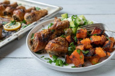 Chicken drumsticks with roasted sweet potatoes and cucumber salad on a plate. Meal for healthy eating, fitness or dieting. Served ready to eat on a plate on white background