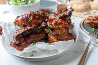 Oven baked or roasted thick pork ribs with homemade barbecue sauce, salad and bread for dinner or lunch on a table