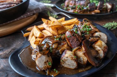 Bratwurst with brown onion, mushroom sauce and homemade french fries on wooden table. Closeup and front view