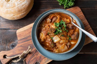 Brown beef stew with cabbage and vegetables. Served with homemade ciabatta bread on wooden table. Top view with space for text