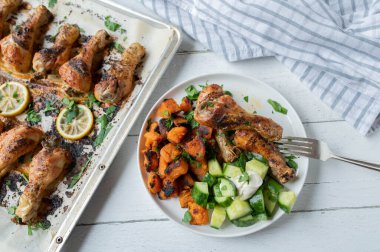 Baked chicken drumsticks with sweet potatoes and cucumber salad on a plate. Healthy low fat dinner or lunch