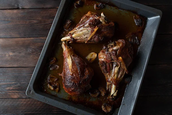 Roasted turkey legs or shanks on a baking sheet isolated on dark wooden background. Flat lay