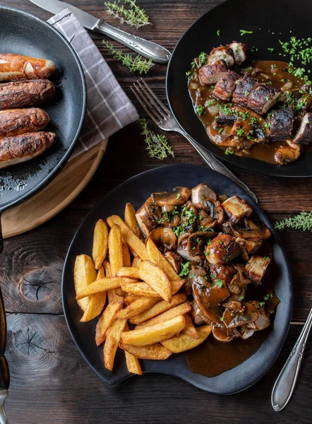 Rustic and savory sausage dish with pan fried german bratwurst, onion mushroom sauce and homemade french fries  on a wood table with plates and pan. Flat lay