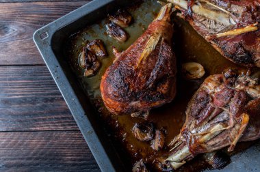 Oven roasted turkey legs on a baking tray isolated on dark wooden background. Table top view