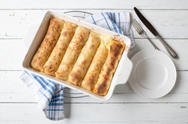 Sweet pancake casserole with quark, lemon filling in a white baking dish on white wooden background. Flat lay