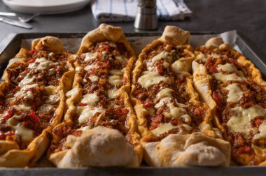 Homemade turkish pide with meat, vegetables and cheese on kitchen table. Closeup and front view