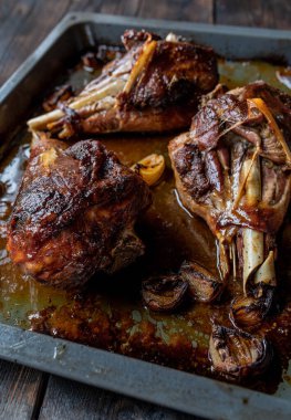Delicious oven baked or roasted turkey legs. Served hot and ready to eat on a baking pan isolated on dark wooden background. Delicious meat dish for sundays or holidays