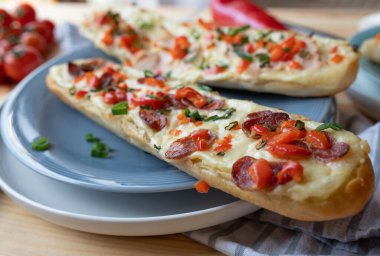 İspanyol salamı, erimiş peynir, Choppe Bell biberi ve soğanlı ev yapımı lezzetli, açık yüzlü salam ekmeği. Sıcak servis edildi ve mutfak masasının arkasındaki tabakta yemeye hazır. Yakın plan, ön görünüm, ön plana odaklan