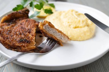 Parmesan peynirli İtalyan usulü domuz pirzolası. Tabakta taze polenta ile servis edilir.