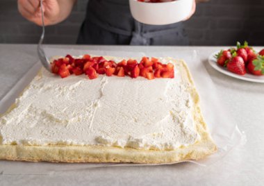 Bir İsviçre böreğini çırpılmış krema ve kadın eli mutfak tezgahında doğranmış çilekle doldurmak.