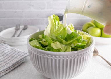 Beyaz kasede yeşil bir salatanın üzerine salata sosu dök.